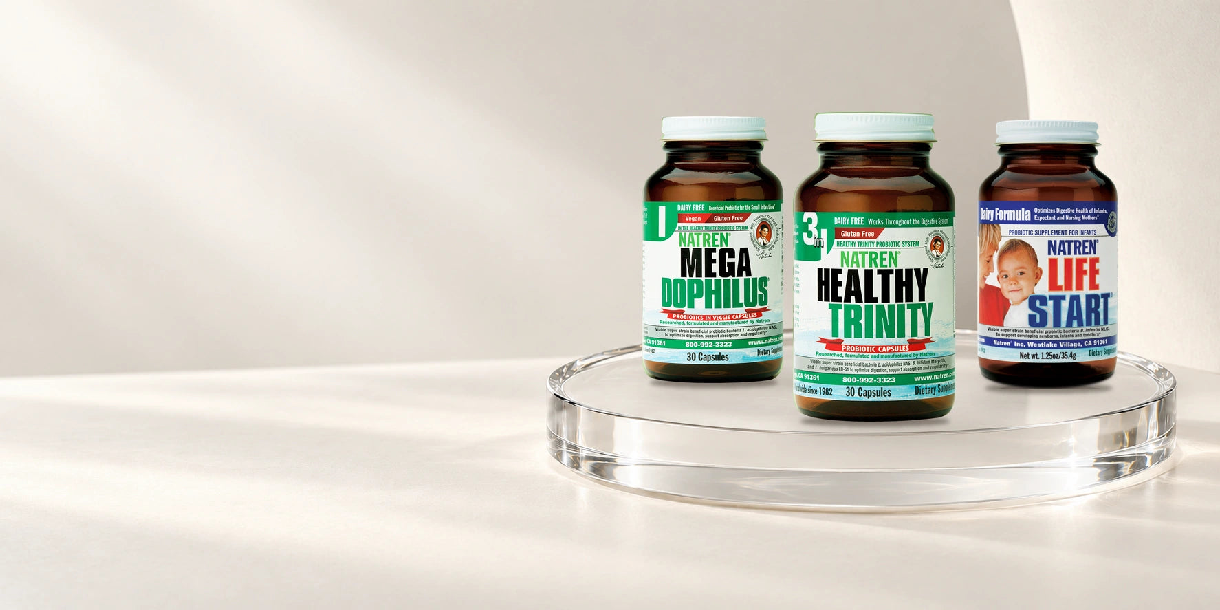Healthy Trinity, Megadophilus and Life Start in their familiar Natren packaging, arranged on a luminous glass platform.
